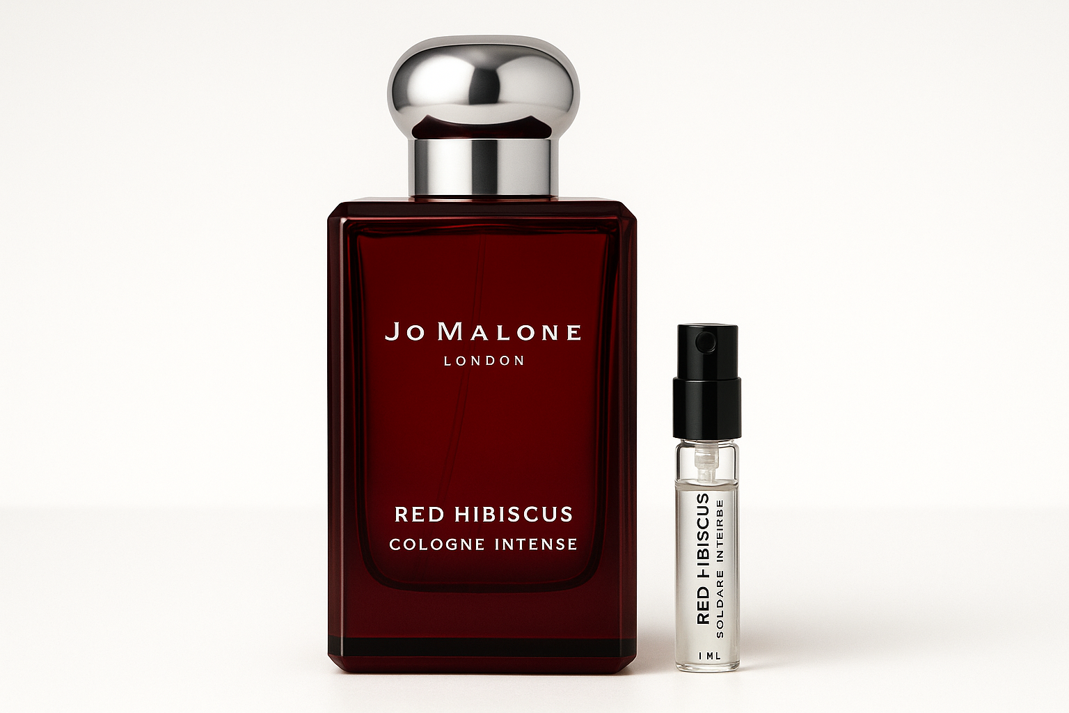 Δείγμα 1ml Jo Malone Red Hibiscus Cologne Intense δίπλα σε μπουκάλι αρώματος 100ml Jo Malone Red Hibiscus Cologne Intense με λευκή γραφή σε σκούρο κόκκινο μπουκάλι