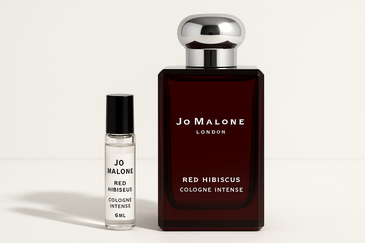Δείγμα Jo Malone Red Hibiscus Cologne Intense 6ml που στέκεται δίπλα σε μπουκάλι αρώματος 100ml Jo Malone Red Hibiscus Cologne Intense με λευκή γραφή σε σκούρο κόκκινο μπουκάλι